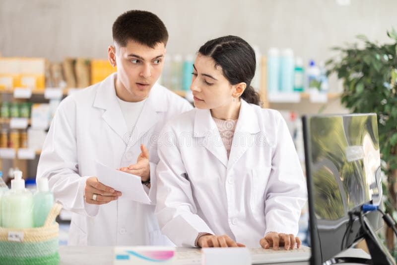 To farmaceuter i hvide kitler diskuterer dokumenter ved en skranke i et apotek.