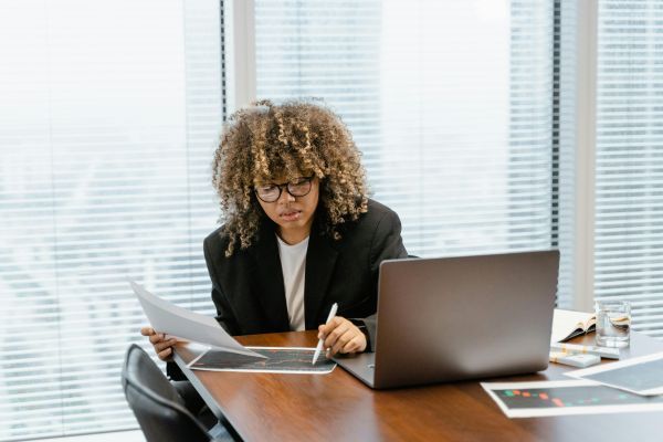 Kvinde gennemgår dokumenter ved et skrivebord med bærbar computer, relateret til international inkasso.