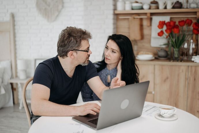 Par taler sammen ved et spisebord med laptop og papirer